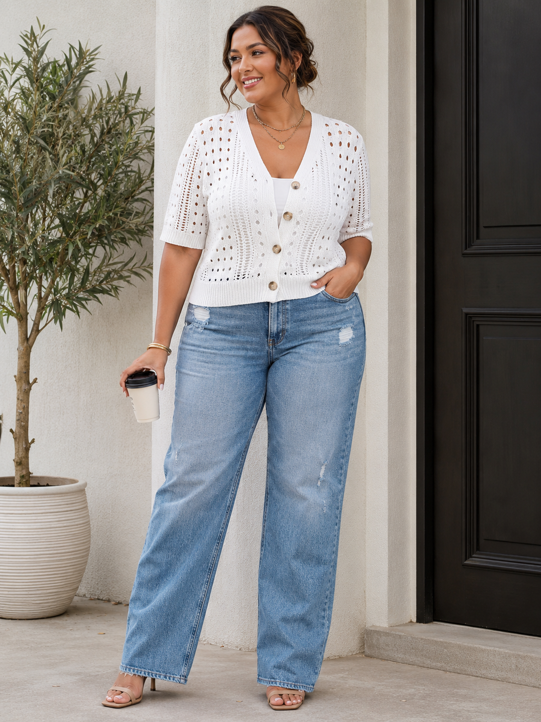 Woman wearing a white crochet top and blue jeans standing in front of a black door.