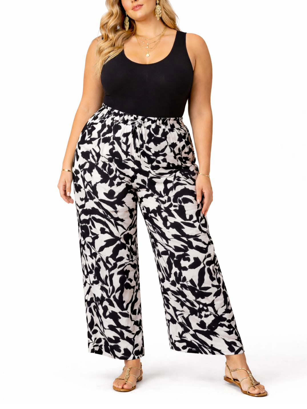 Woman wearing a black tank top and white patterned pants on a white background
