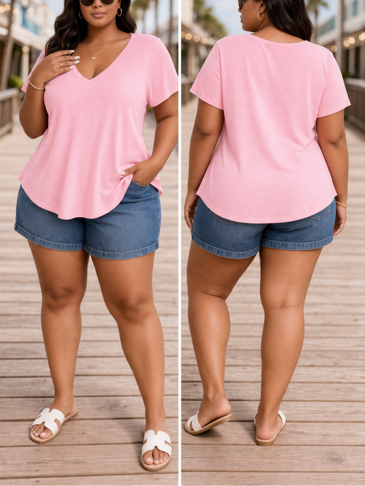 Woman wearing a pink top and denim shorts on a wooden deck with palm trees in the background.